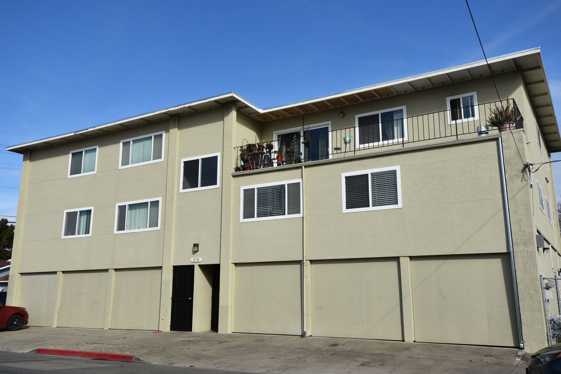 Three-story beige apartment building with garage doors and balconies on a sunny day