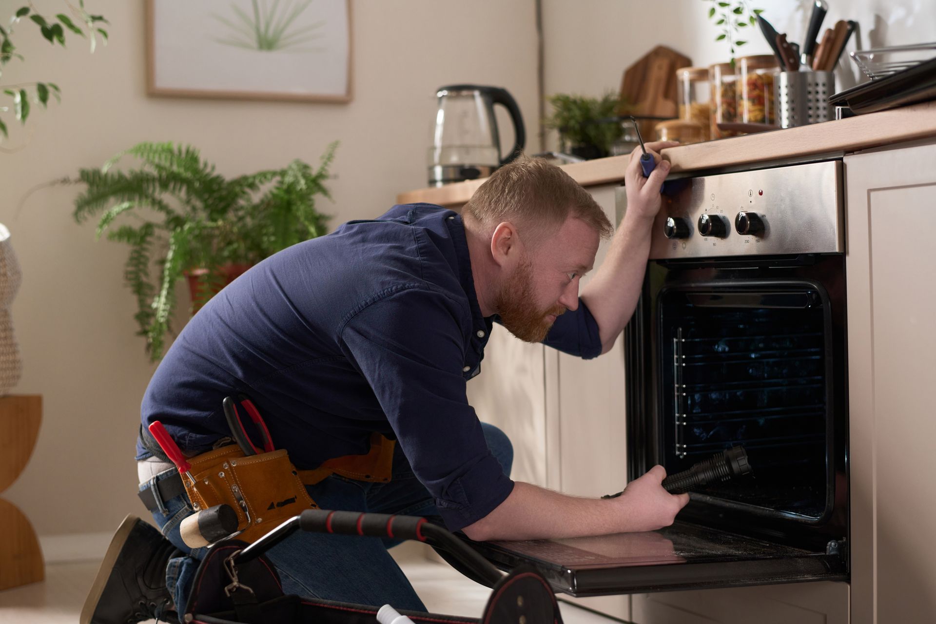 a man is kneeling down in a kitchen fixing an oven .
