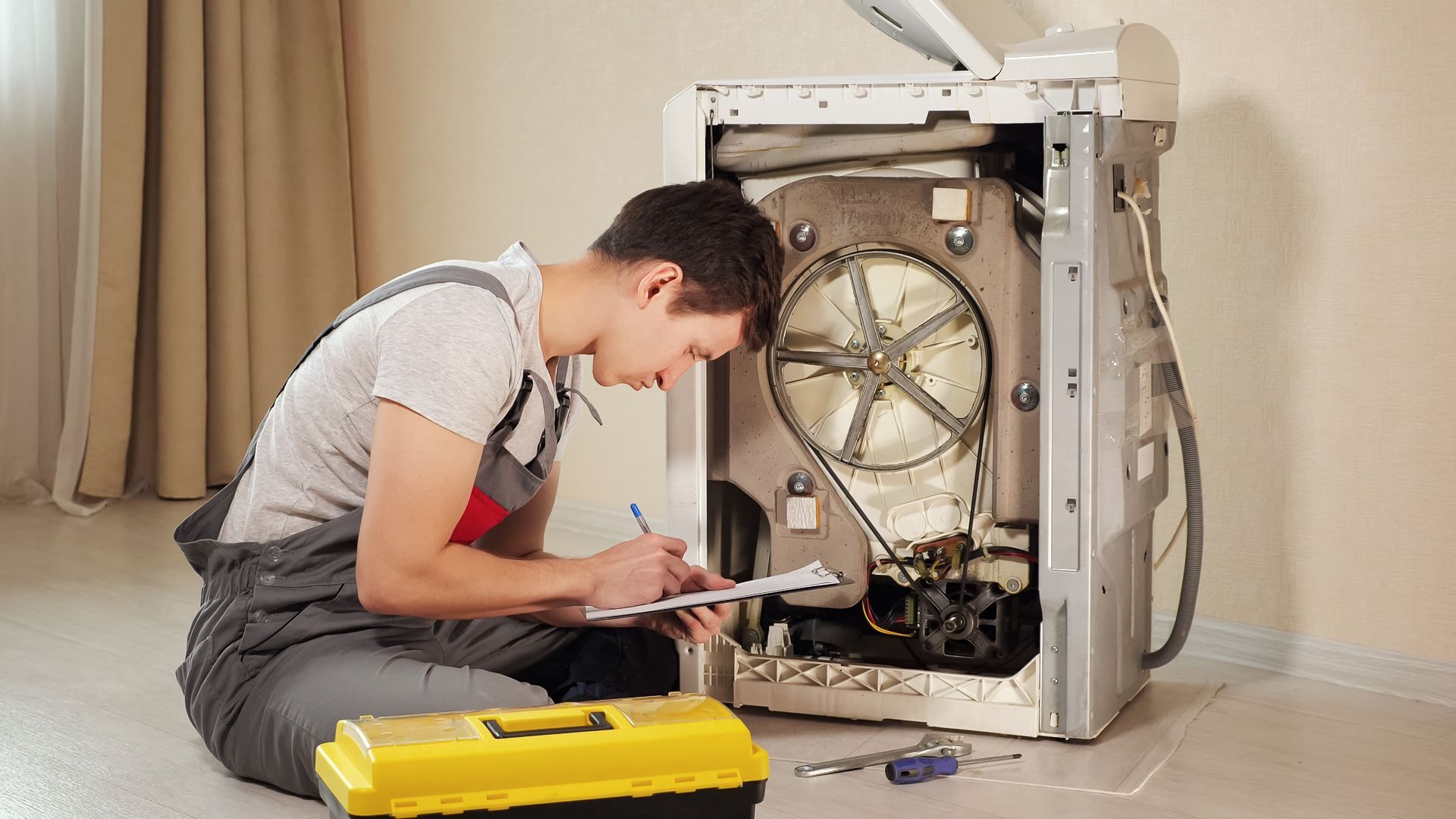 a man is sitting on the floor fixing a washing machine .