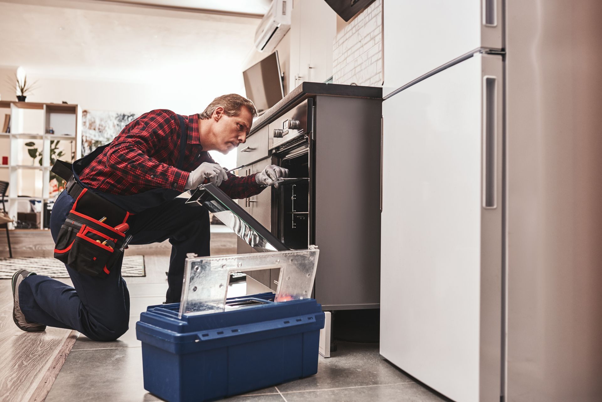 a man is kneeling down in a kitchen fixing an oven .