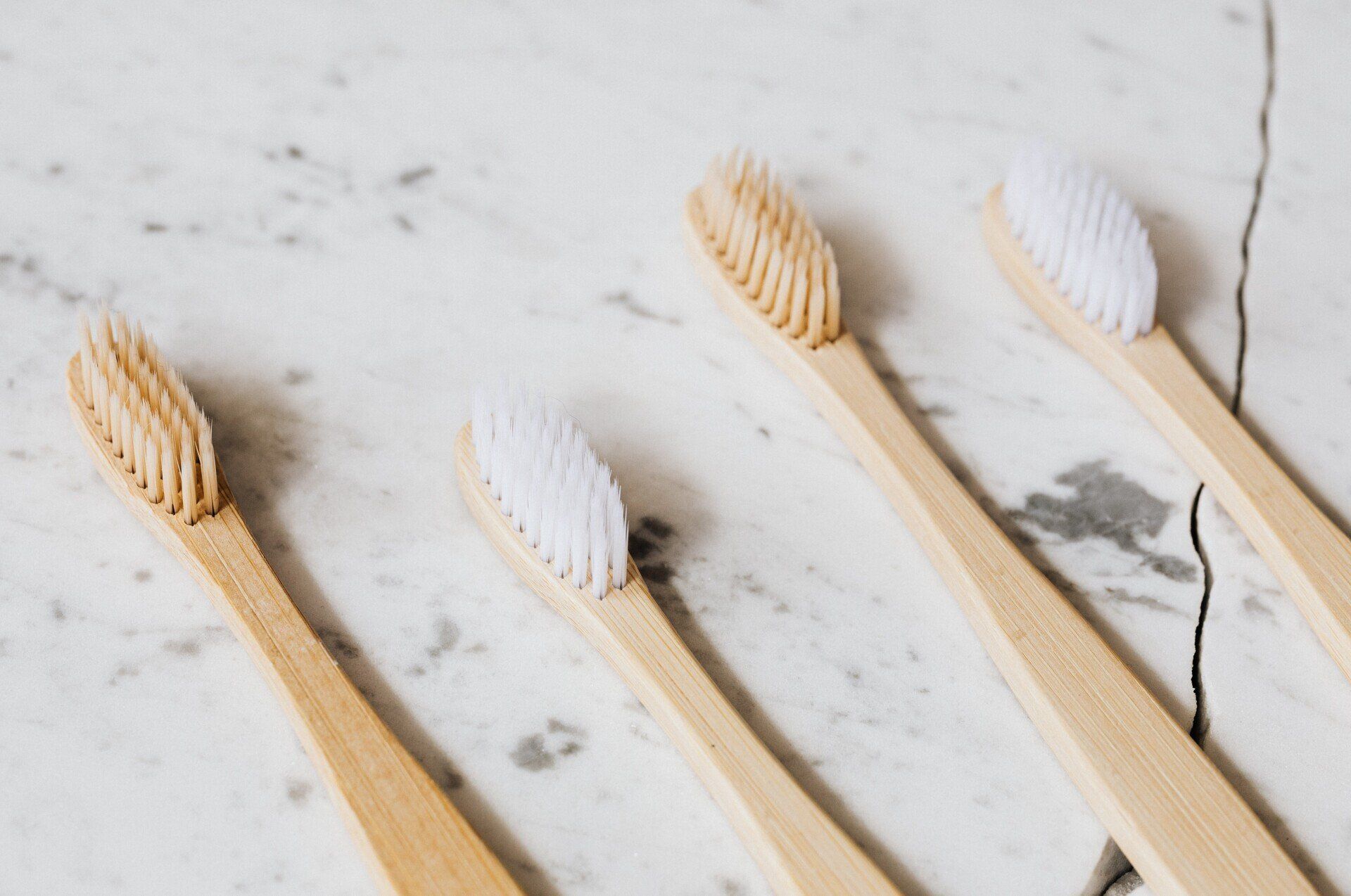 Four bamboo toothbrushes with white and tan bristles on a white marble surface