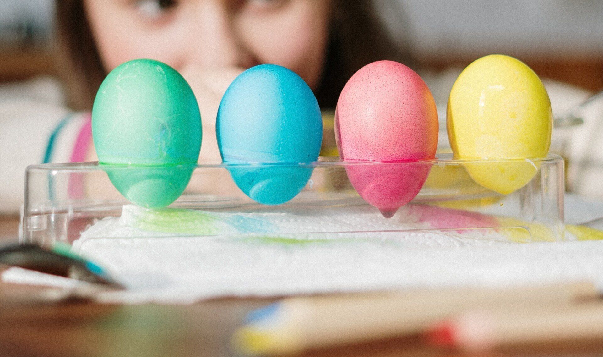Four colorful Easter eggs standing upright in a glass dish on a table.
