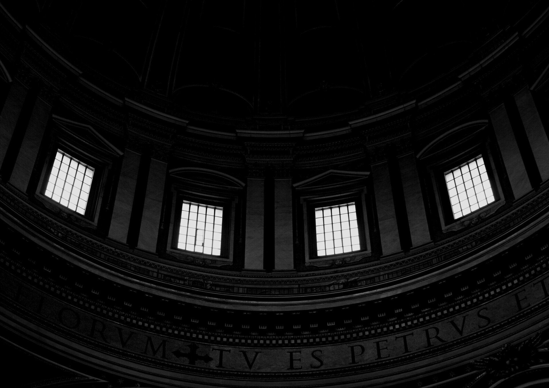 Dim view of a domed interior ceiling with arched windows and ornate molding