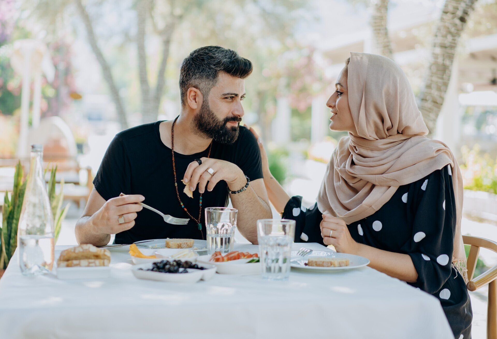 Two people chatting at an outdoor café table, with drinks and plates in front of them.