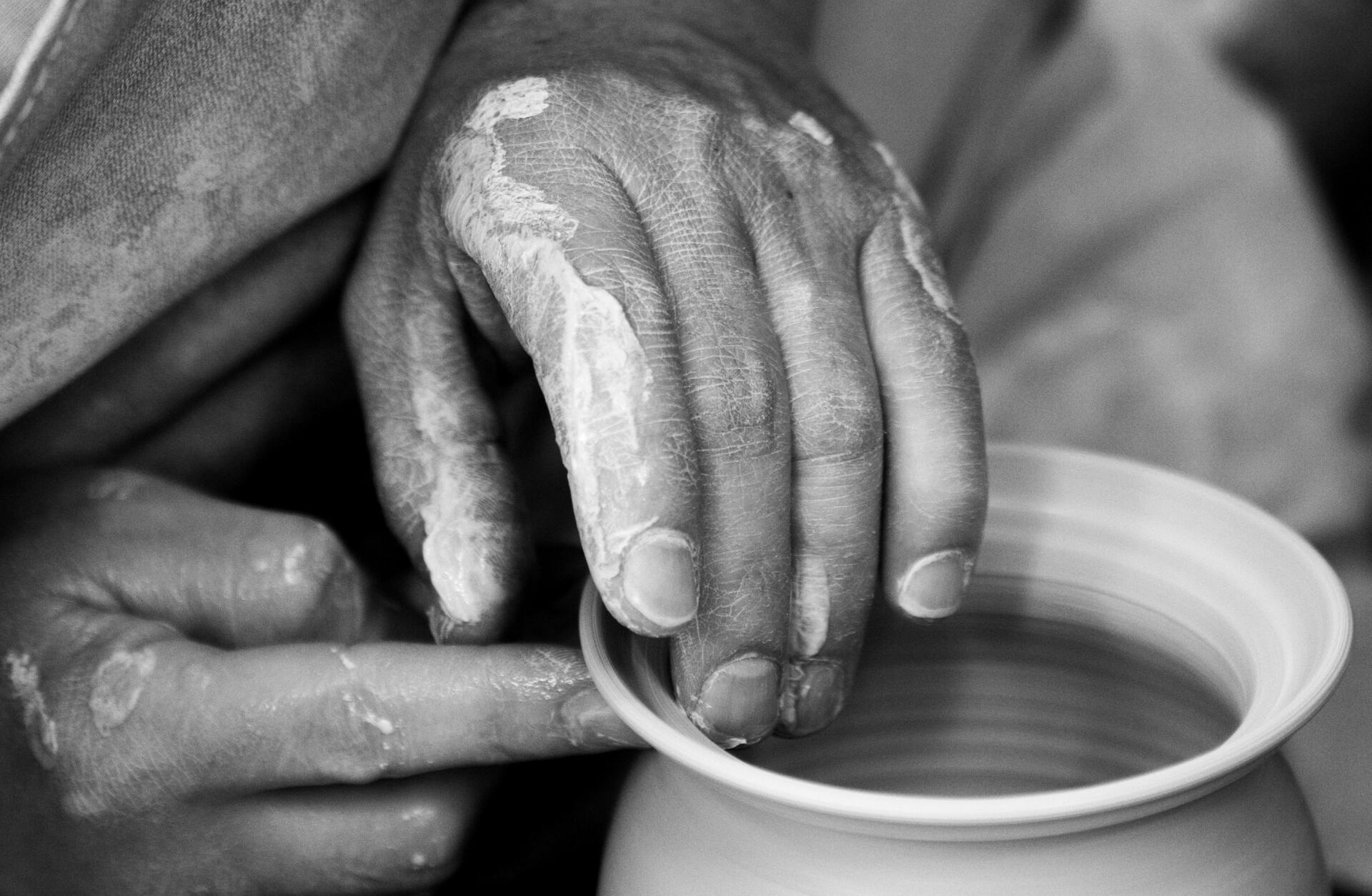 Hands dipping fingers into a small bowl of water, close-up in black and white.