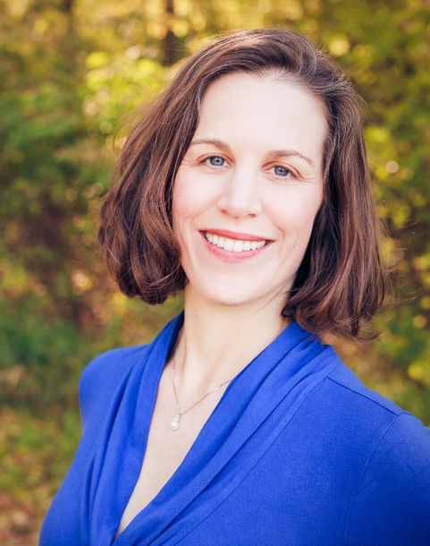 Smiling person in a blue top outdoors with blurred greenery in the background