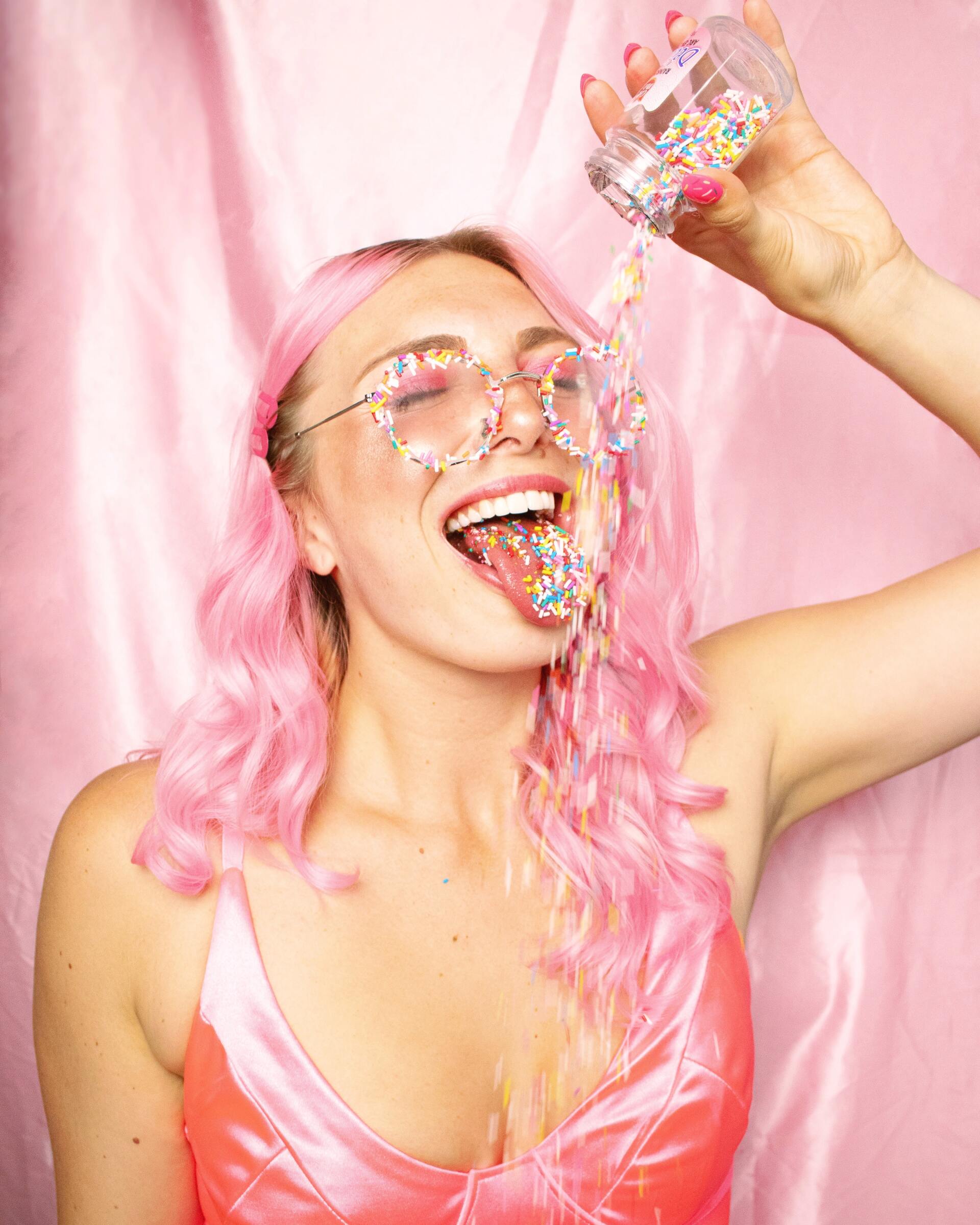Woman with pink hair laughing as colorful confetti falls against a pink backdrop