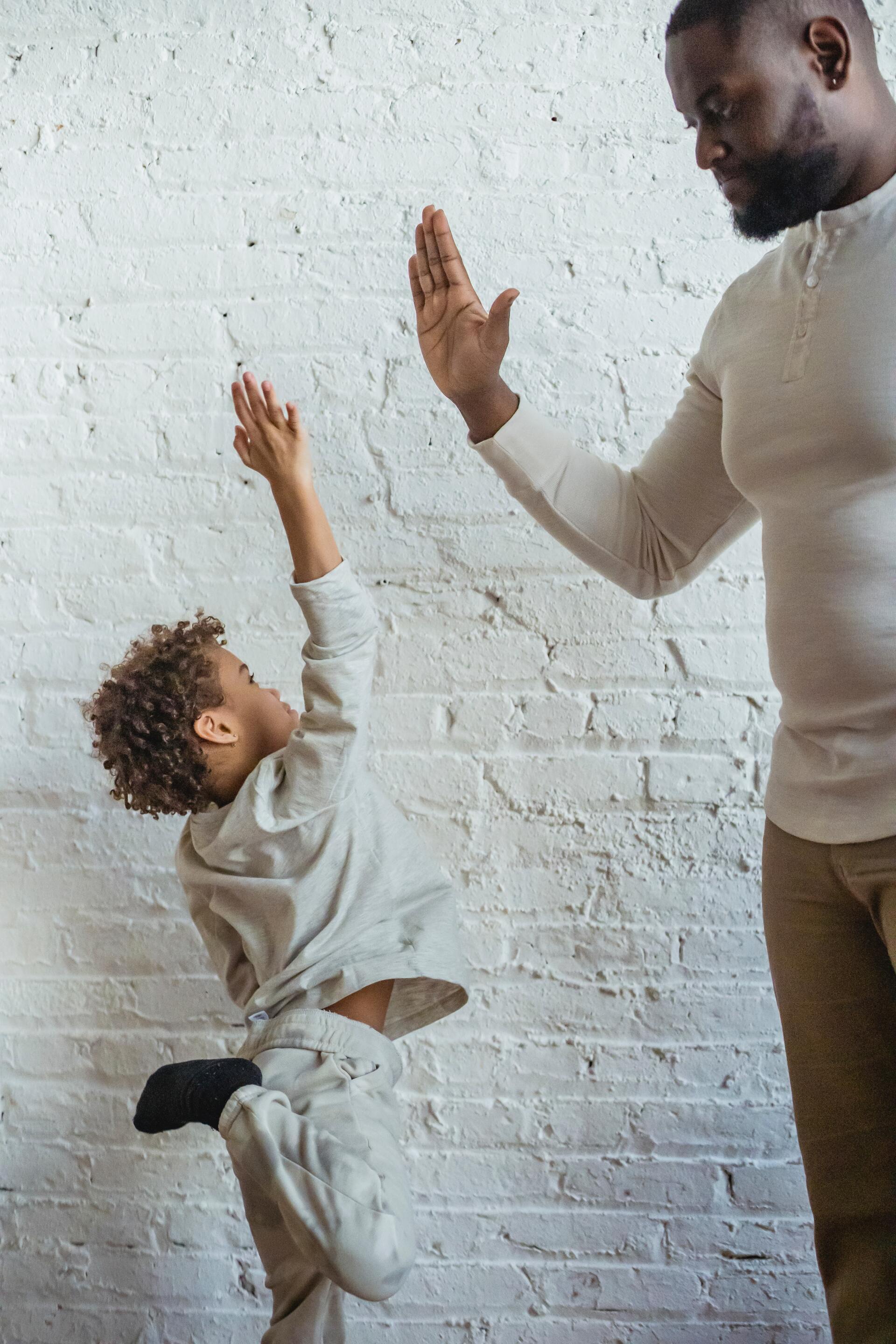 Adult and child reaching up for a high-five against a white brick wall