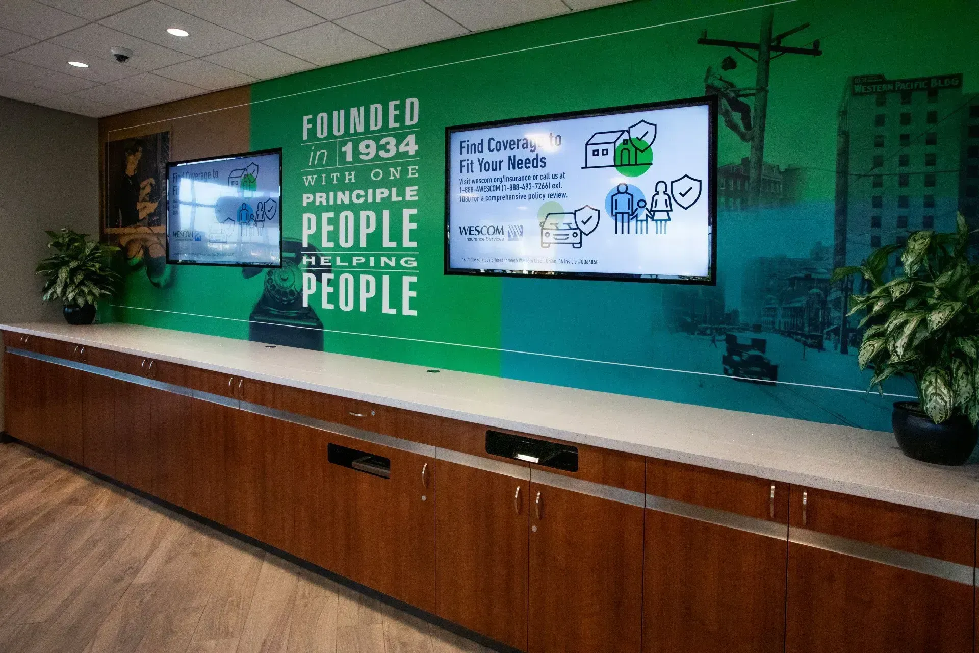 Modern lobby with green wall, long wooden counter, and two wall-mounted screens displaying graphics