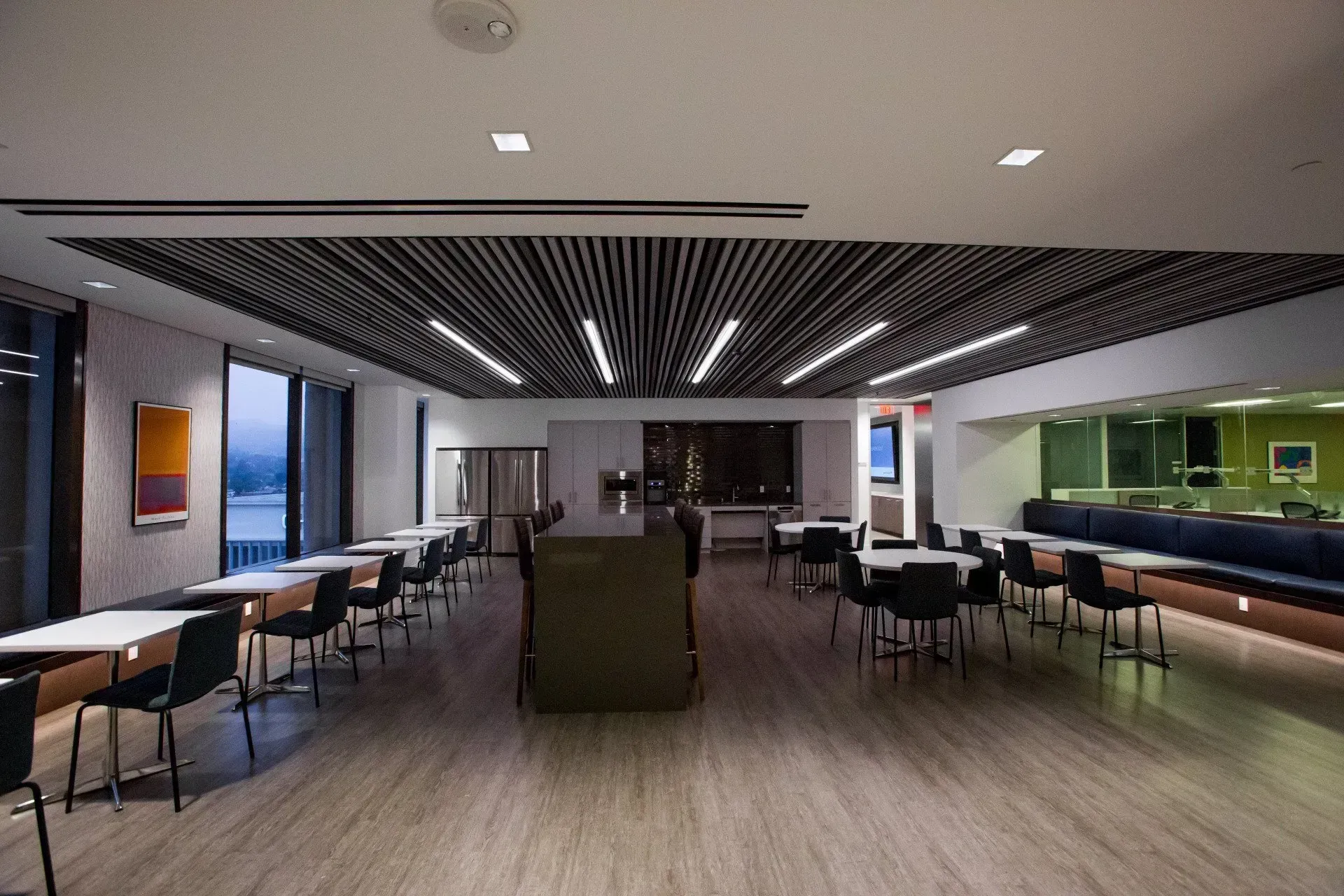 Modern lounge with tables, chairs, green booths, and a central seating area under a slatted ceiling.