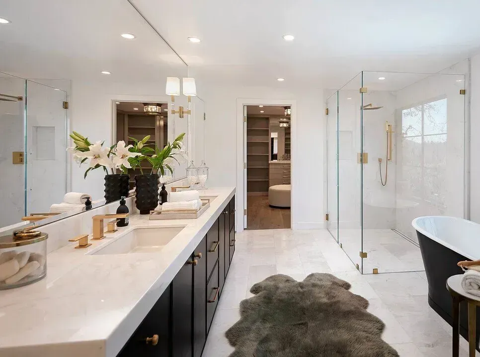 Bright modern bathroom with double vanity, glass shower, black tub, and gray rug