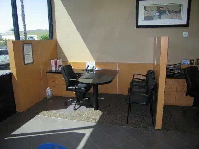 Small booth seating area in a restaurant with dark chairs, a round table, and sunlight on the floor.