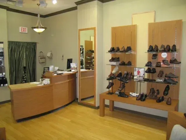 Shoe store interior with wooden displays, mirror, counter, and rows of shoes on shelves.