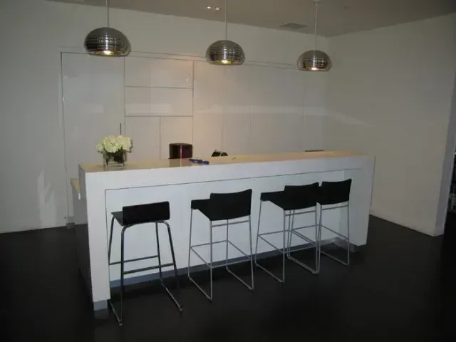 Modern white bar counter with three black stools and hanging pendant lights in a minimalist room