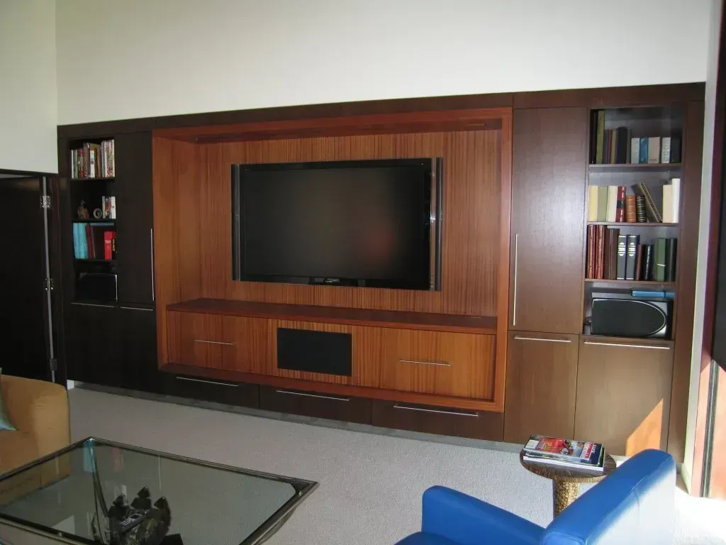 Living room with a wall-mounted TV in a wood entertainment center, glass coffee table, and blue chair