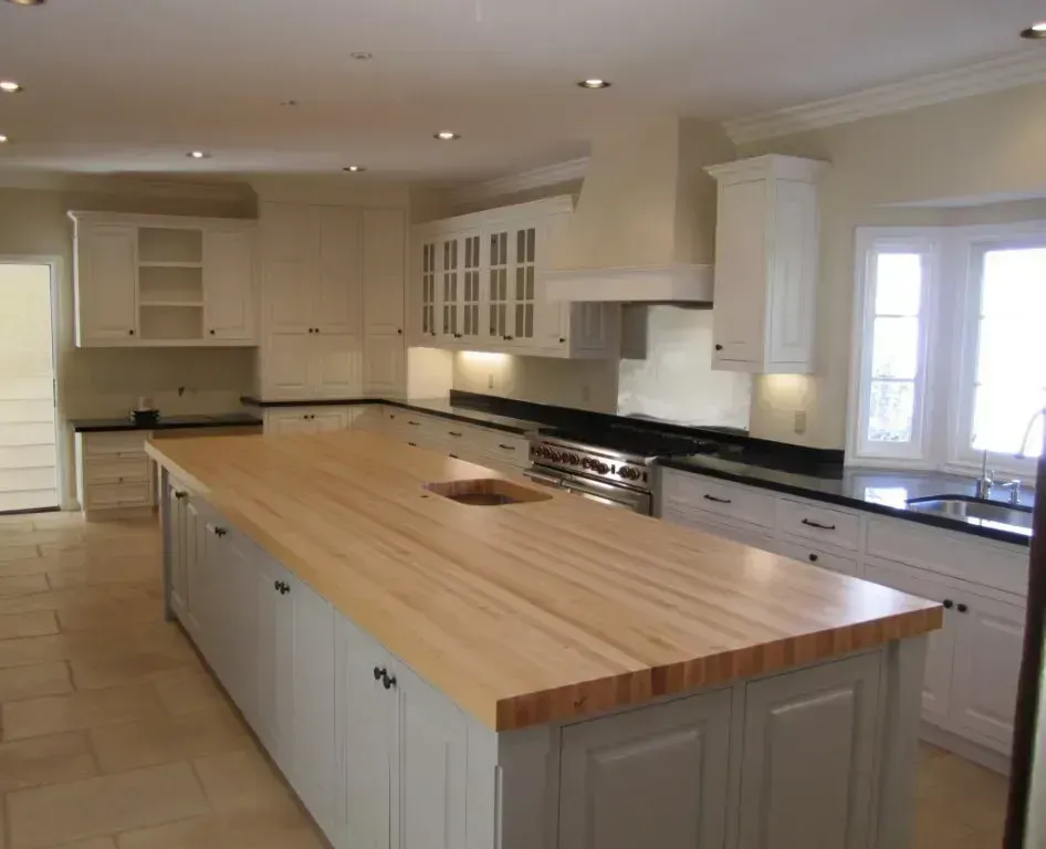 Bright kitchen with a large butcher-block island and white cabinets, viewed from the corner.