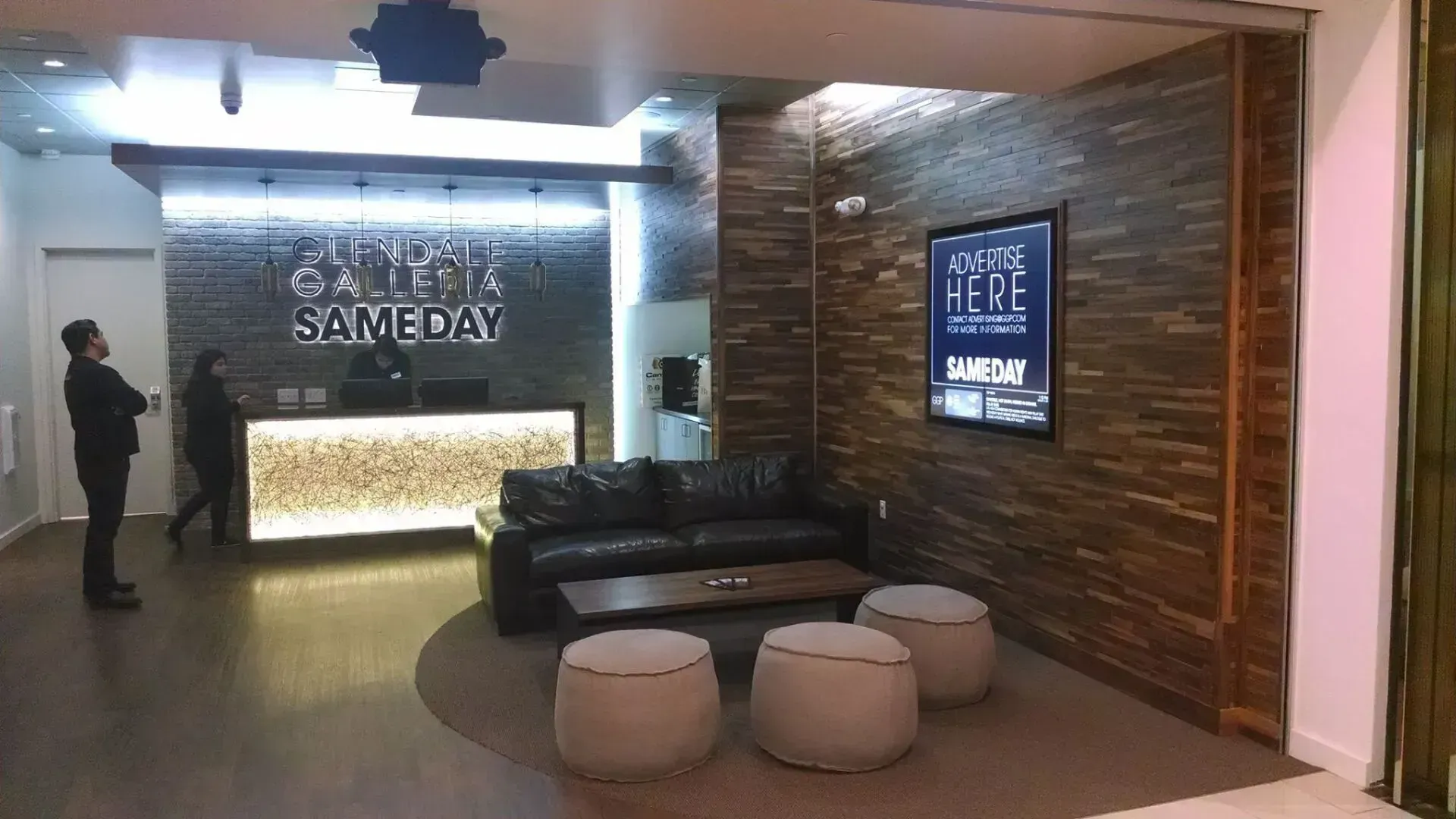 Modern lobby with a black couch, round ottomans, illuminated wall sign, and a digital display