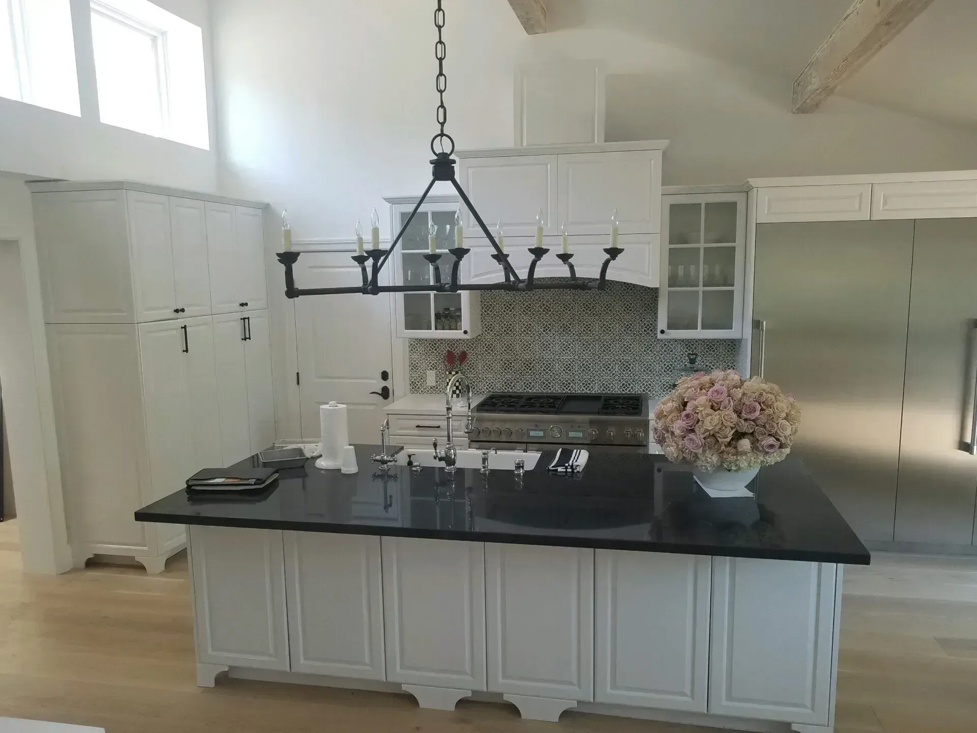 Modern white kitchen with black island countertop, pendant lights, stainless fridge, and flower centerpiece