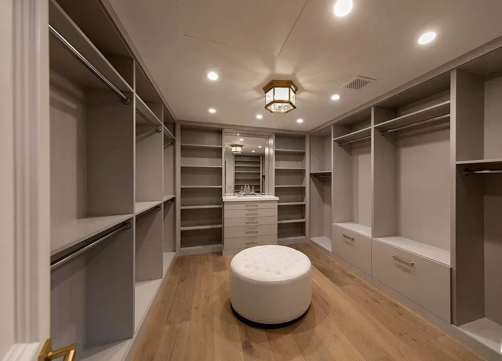 Spacious walk-in closet with built-in shelves, gray walls, wood floor, and a round ottoman in the center