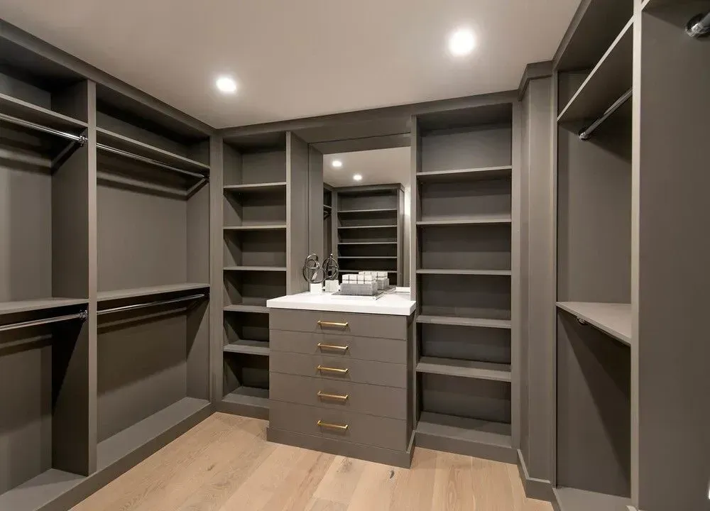 Gray walk-in closet with built-in shelves, hanging rods, drawers, and light wood floor.