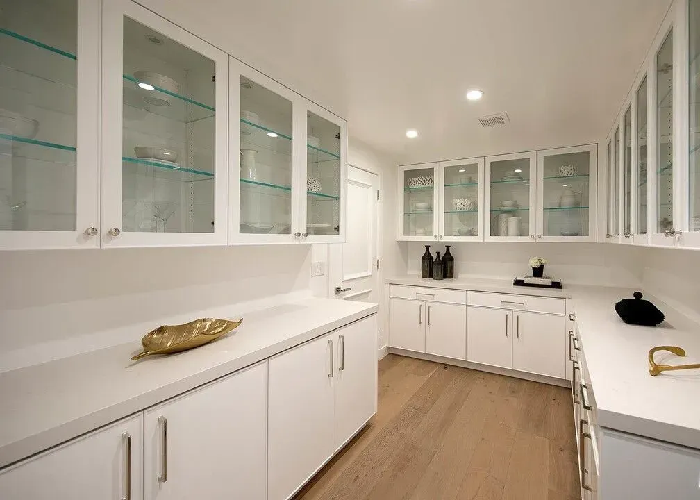 Bright white modern kitchen with glass-front cabinets, light wood floor, and gold accents