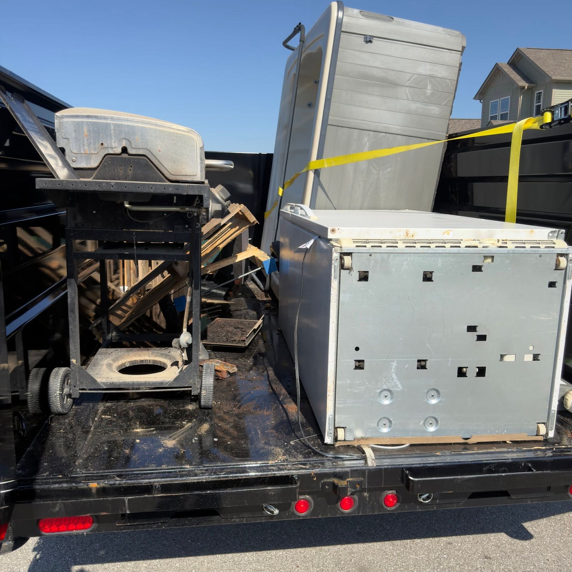 Flatbed trailer hauling large metal appliances and crates secured with yellow straps under a blue sky.