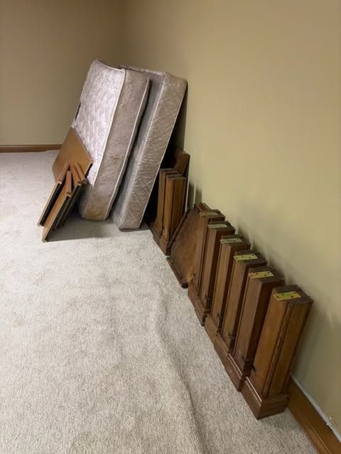 Folded tablecloths and wooden trays stacked against a beige wall on a carpeted floor.