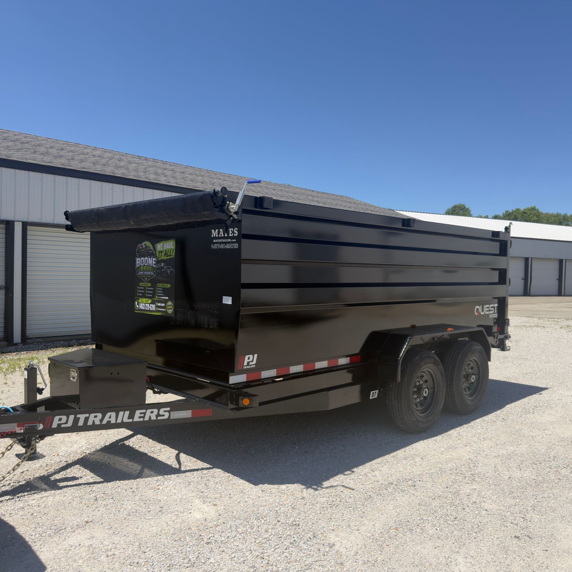 Black dump trailer parked outside a white industrial building under a clear blue sky