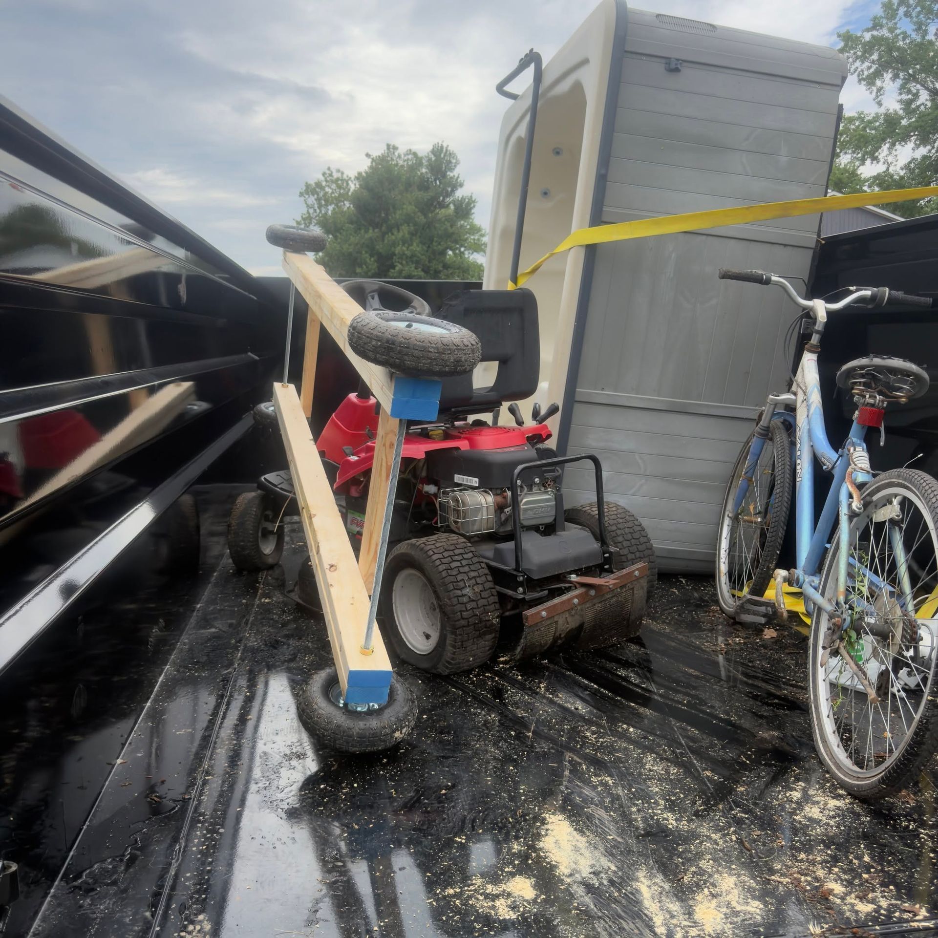 Rain-soaked trailer bed with a small black utility cart, blue bicycle, and yellow tie-down strap.