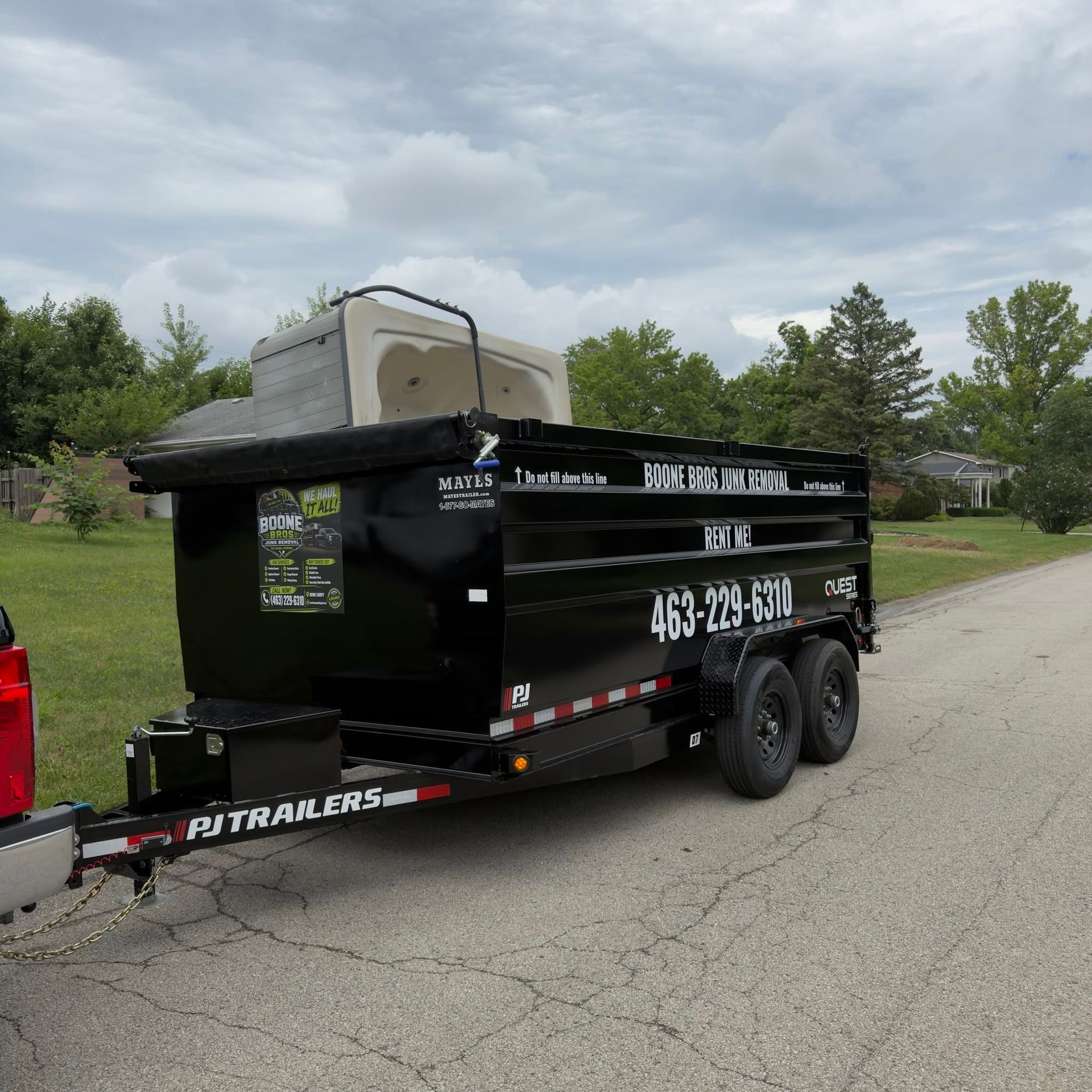 Black dump trailer parked on a residential street, with a silver cargo box on top and company decals.