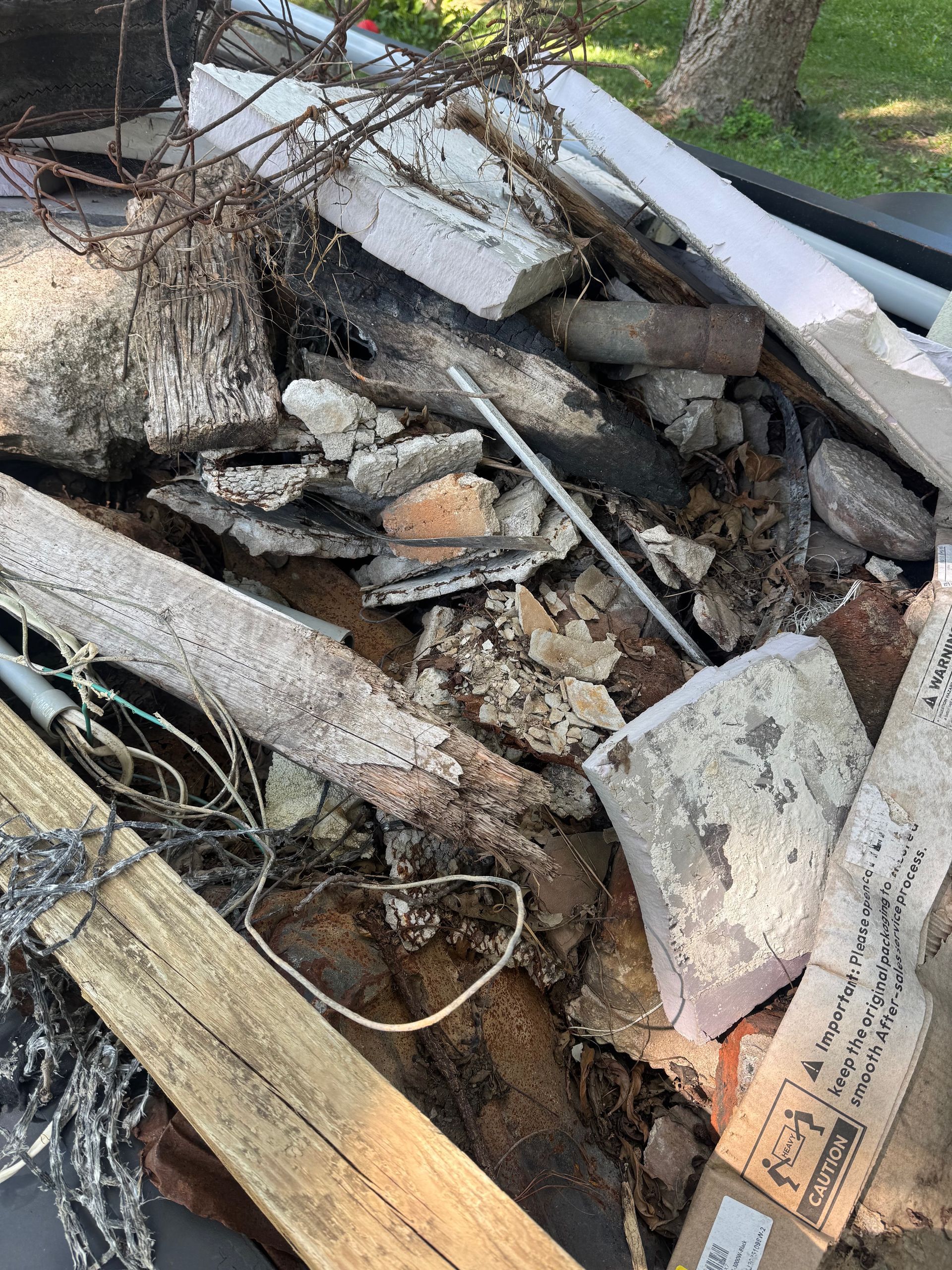 Pile of broken wood, rocks, and debris outdoors near a tree.