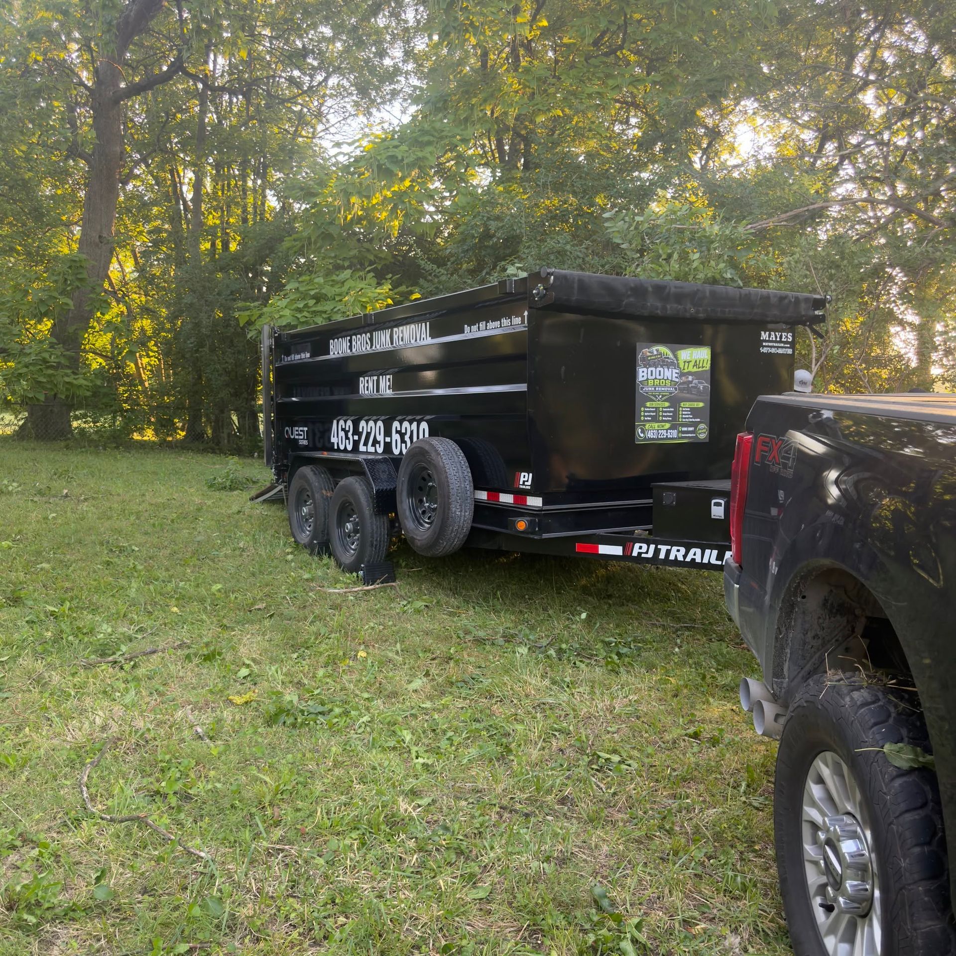 Black enclosed cargo trailer hitched to a truck in a grassy wooded area