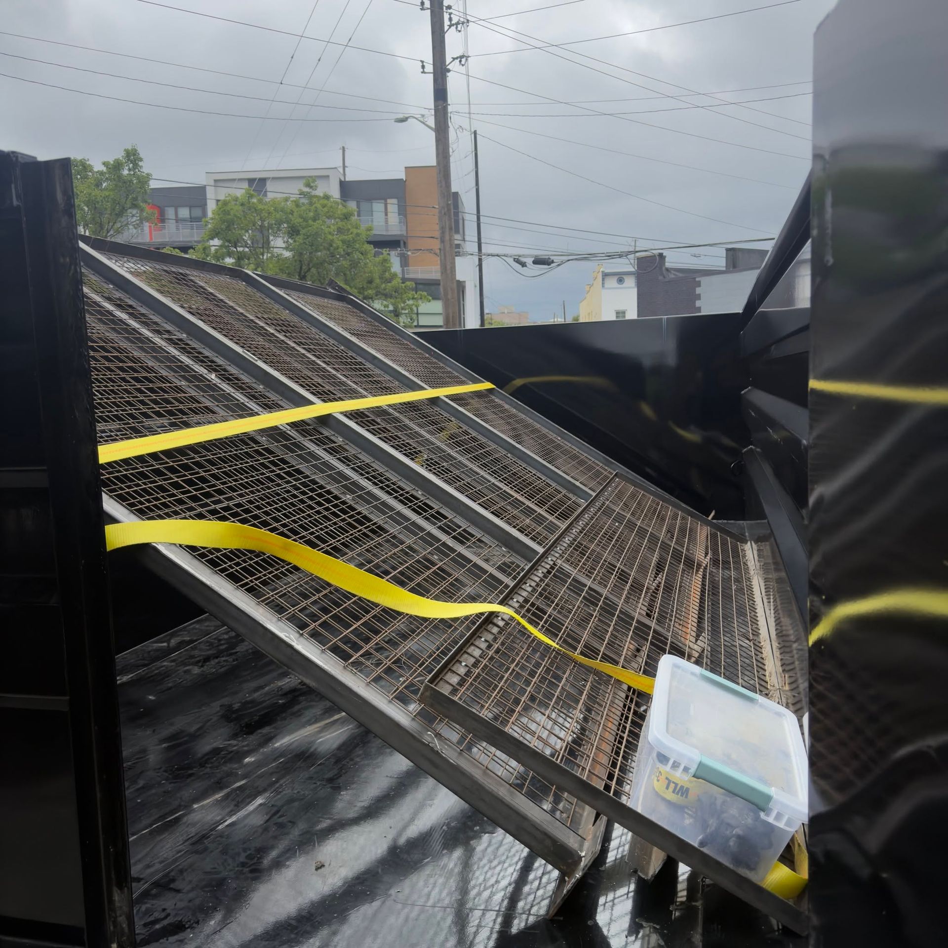 Wavy yellow tape across a damaged metal walkway above train tracks on a rainy day