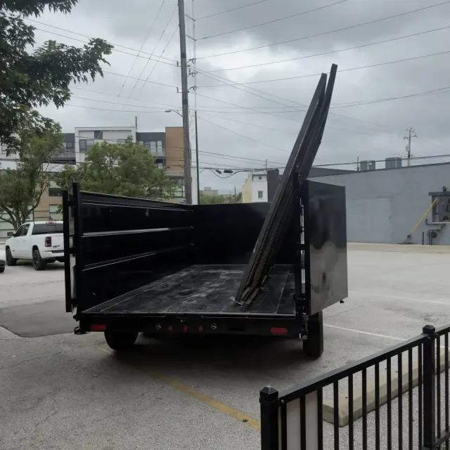Black dump trailer with raised side panels parked in an empty lot under cloudy skies
