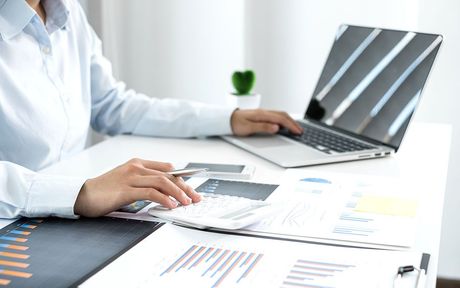 Une femme est assise à un bureau et utilise un ordinateur portable et une calculatrice.