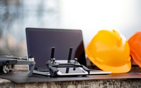 Un ordinateur portable, une télécommande, des casques de sécurité et un drone sont sur une table.