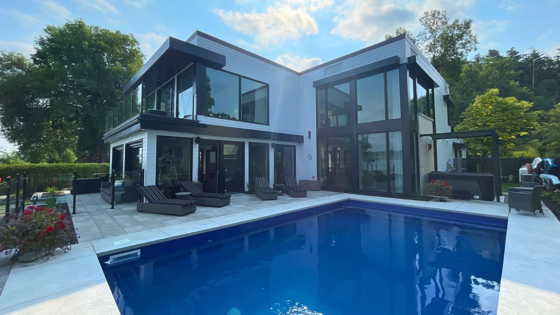 Maison de prestige blanche moderne avec de grandes fenêtres, une piscine extérieure et des arbres en arrière-plan.