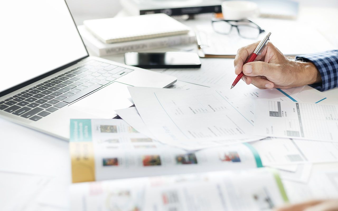 Une personne écrit sur un morceau de papier alors qu'elle est assise à un bureau avec un ordinateur portable.