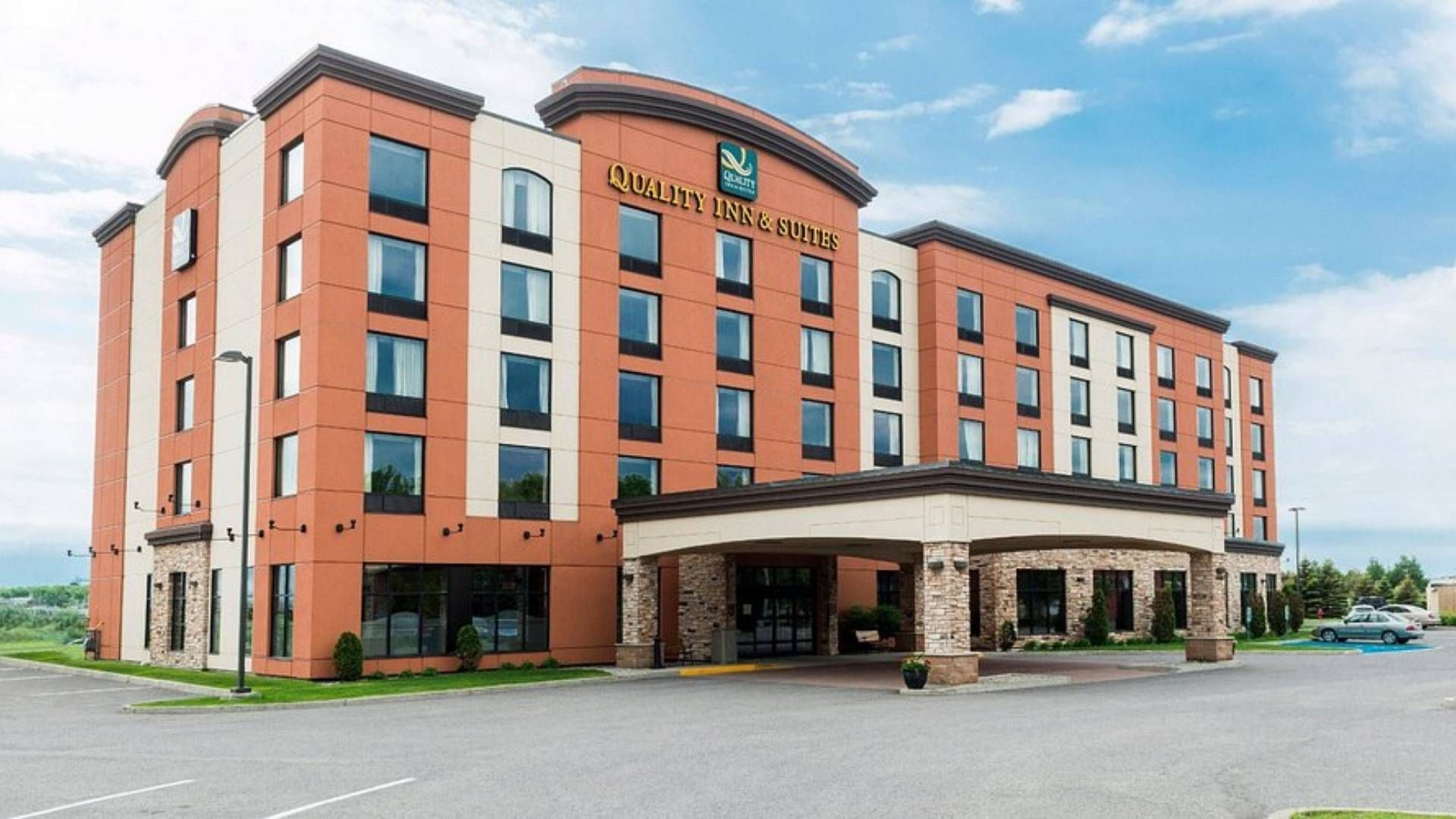Extérieur de l'hôtel Quality Inn and Suites. Bâtiment en briques avec de grandes fenêtres, entrée couverte, ciel bleu.