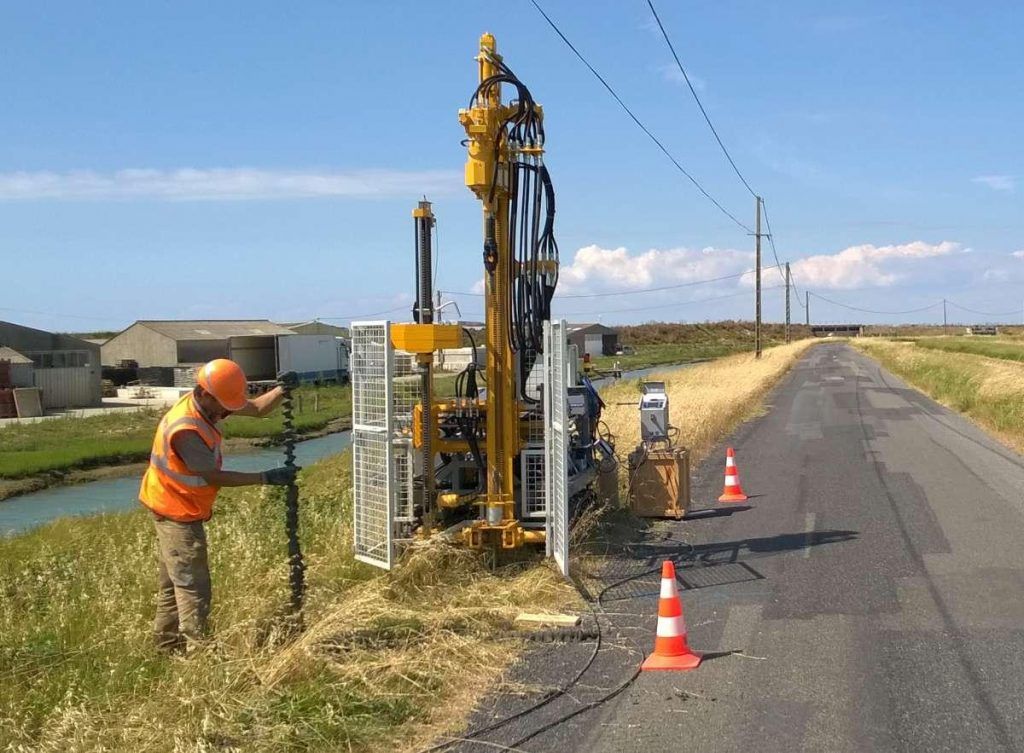 Un homme réalise une étude géotechnique à l'aide d'une machine au bord d'une route.