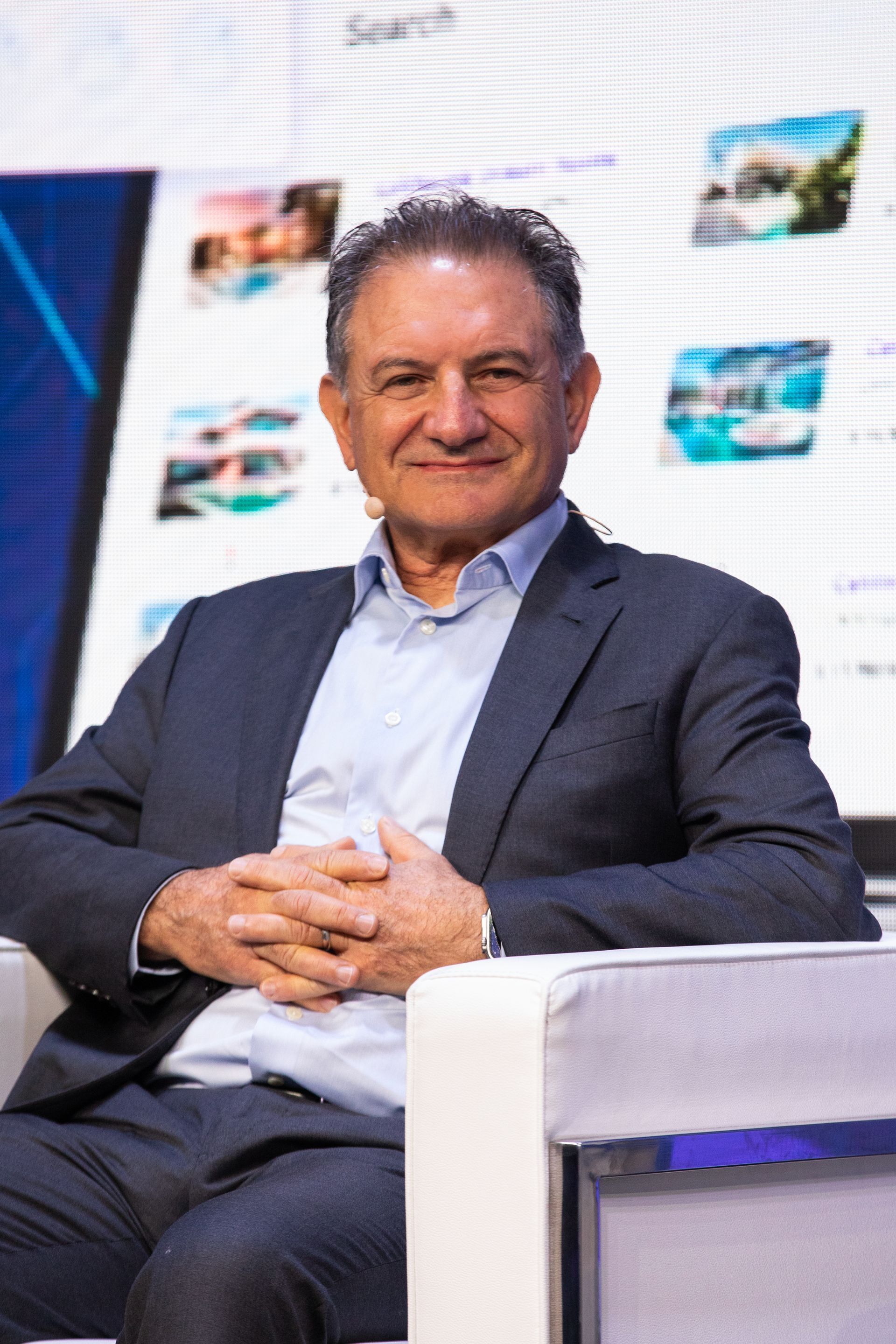 A man in a suit is sitting in a chair with his hands folded.