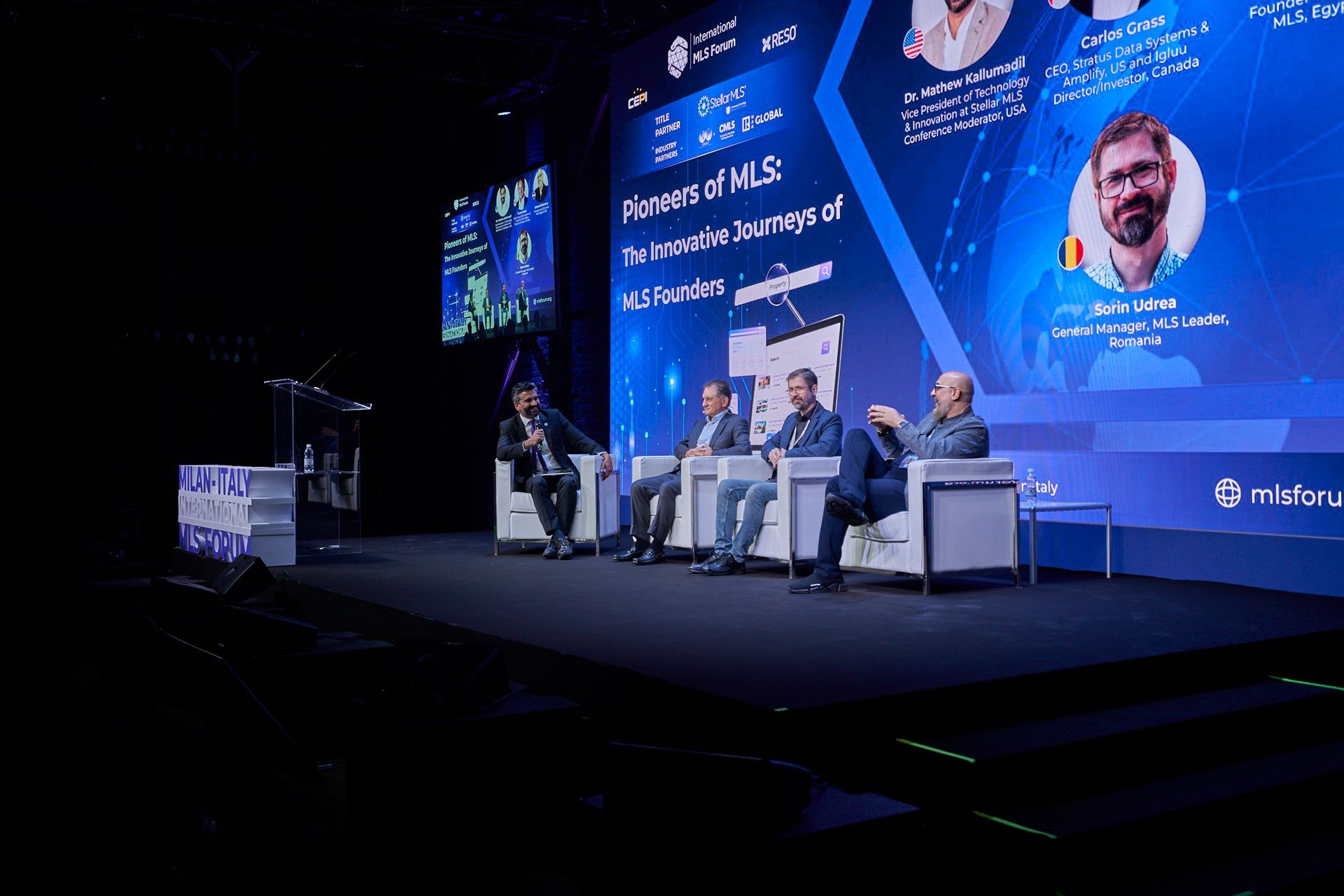 A group of people are sitting on a stage in front of a large screen.