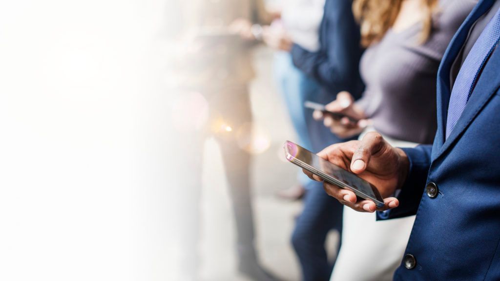 A group of people are standing next to each other looking at their phones.