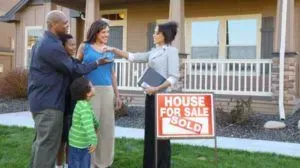 A family is standing in front of a house for sale.