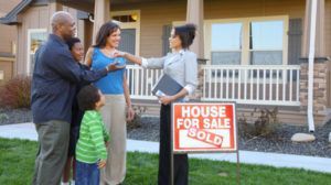 A family is standing in front of a house for sale.
