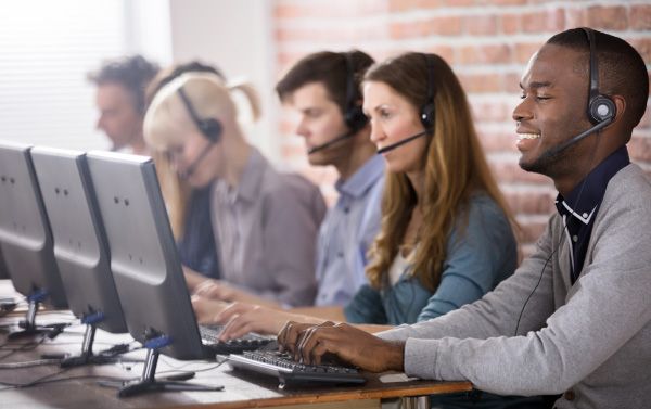 A group of people are sitting in front of computer monitors wearing headsets.