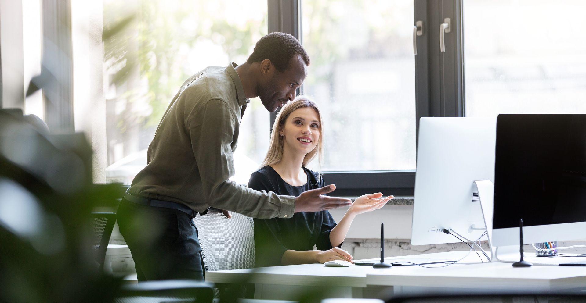 A man and a woman are looking at a computer screen in an office.