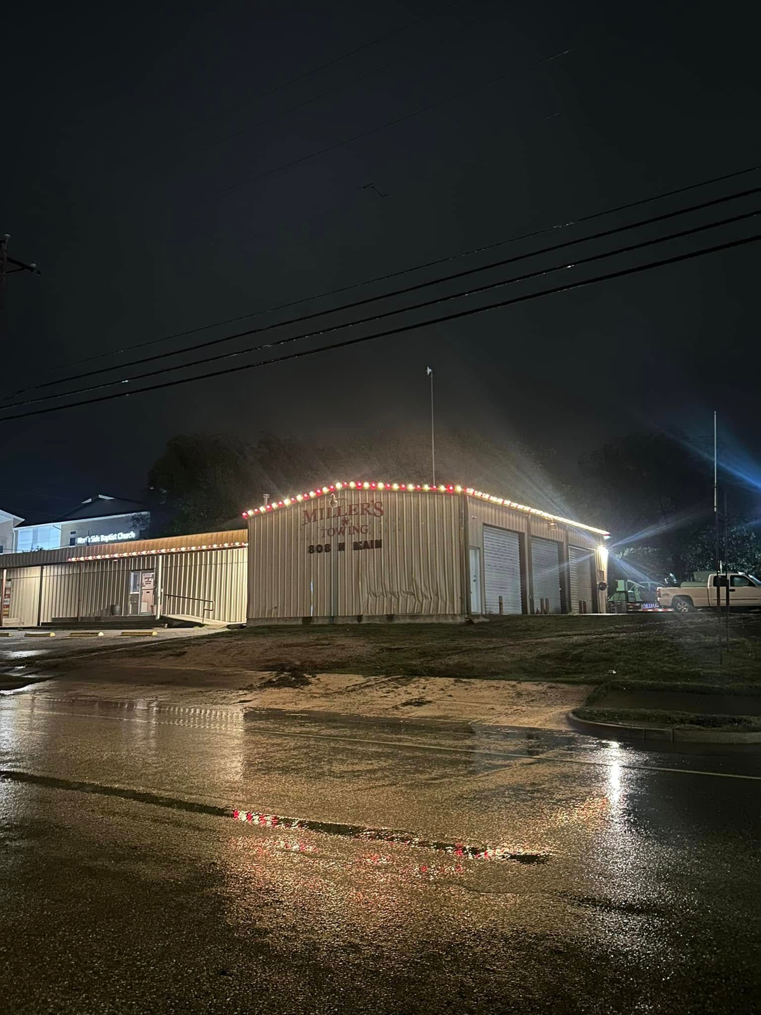 Nighttime view of a lit building reflected in a wet parking lot under dark skies.