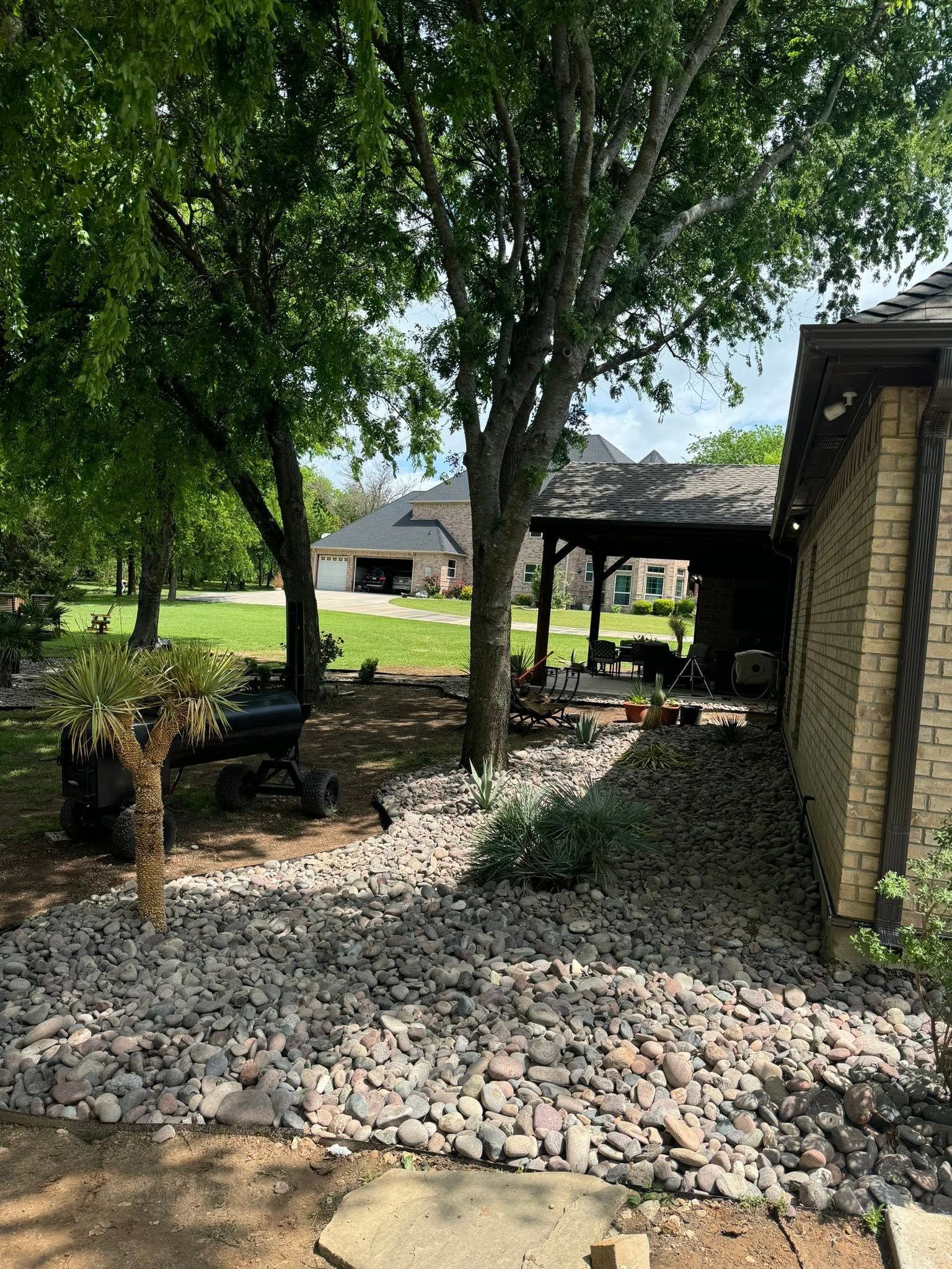 Tree-shaded stone patio with outdoor seating beside a stone building and lawn beyond
