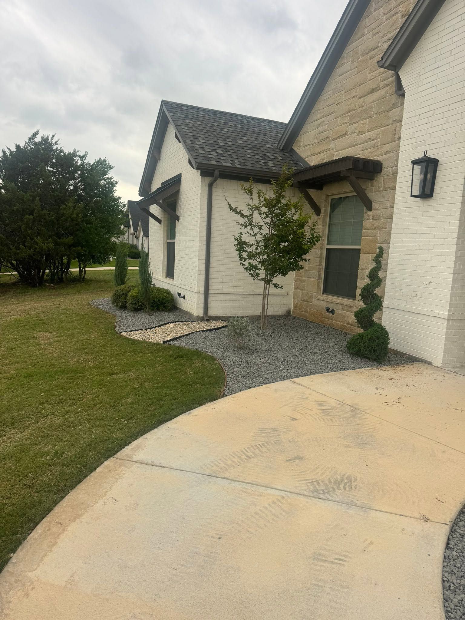 Front view of a white brick house with a curved concrete driveway and landscaped yard